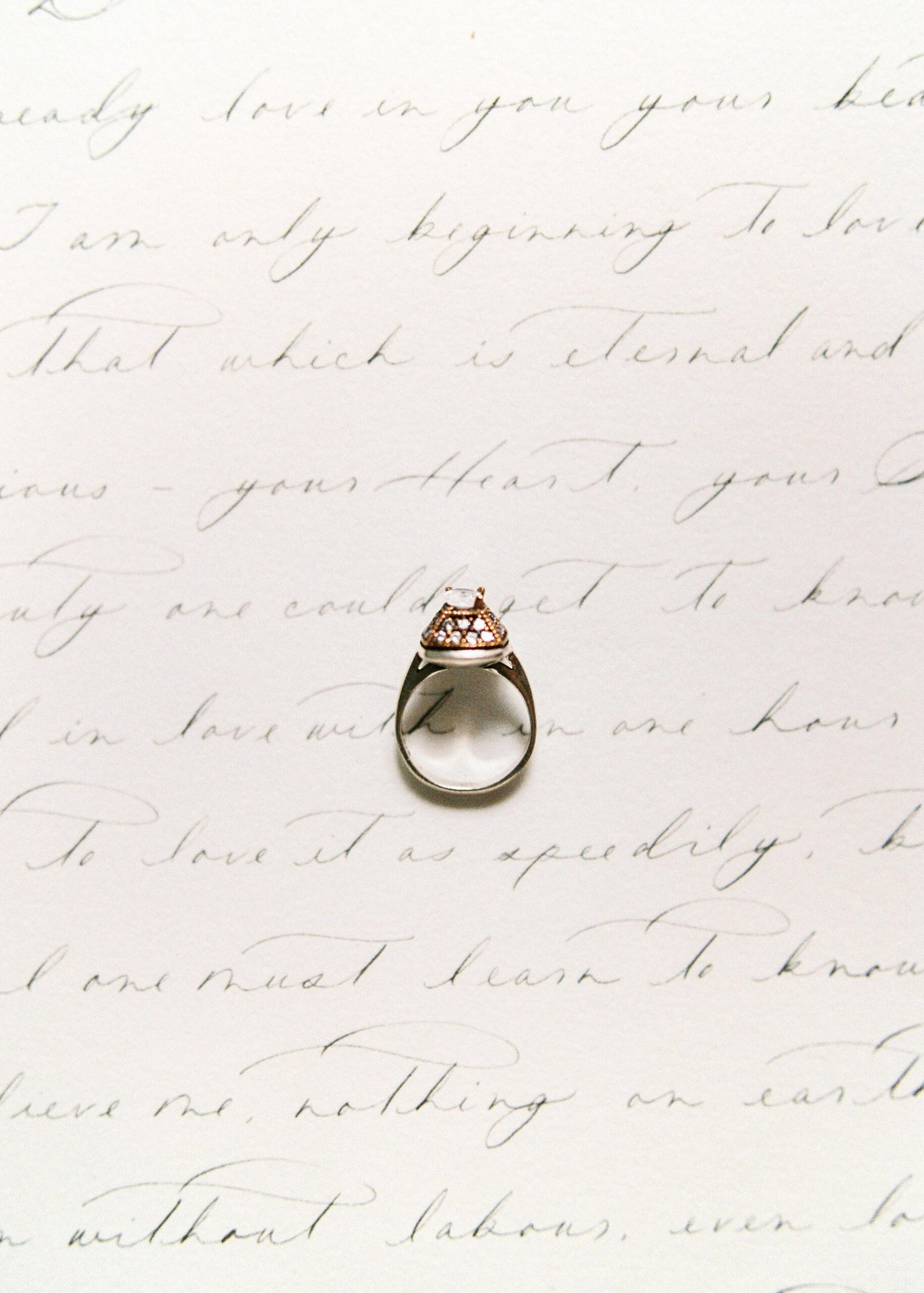 A diamond ring elegantly placed on handwritten calligraphy creates a vintage romantic scene.